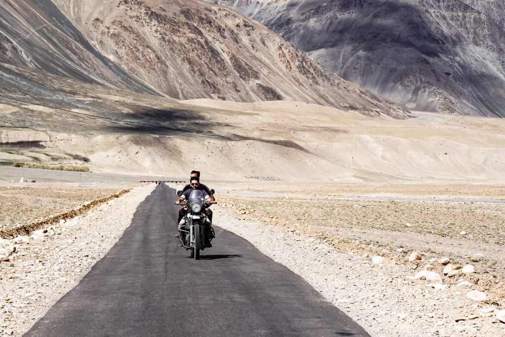 A Man Riding A Motorcycle On A Road Near Hills