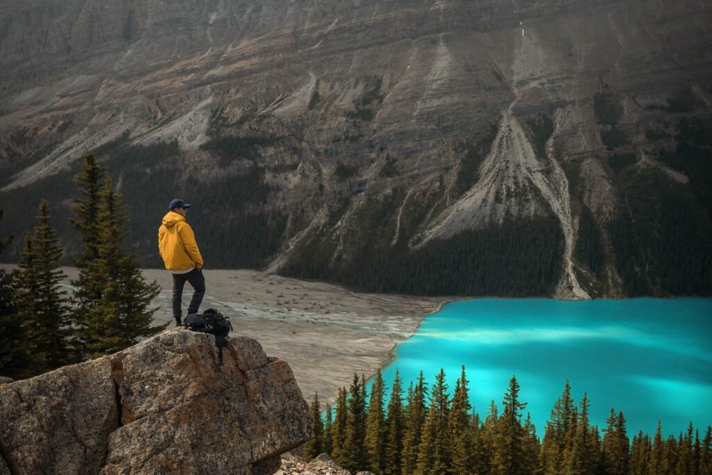 A Man Standing On Gray Stones And Looking Towards A Lake.