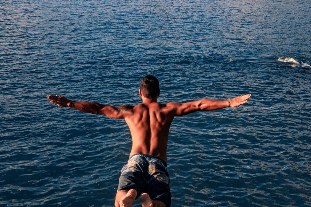 A Fit Young Man Jumping Into Ocean.